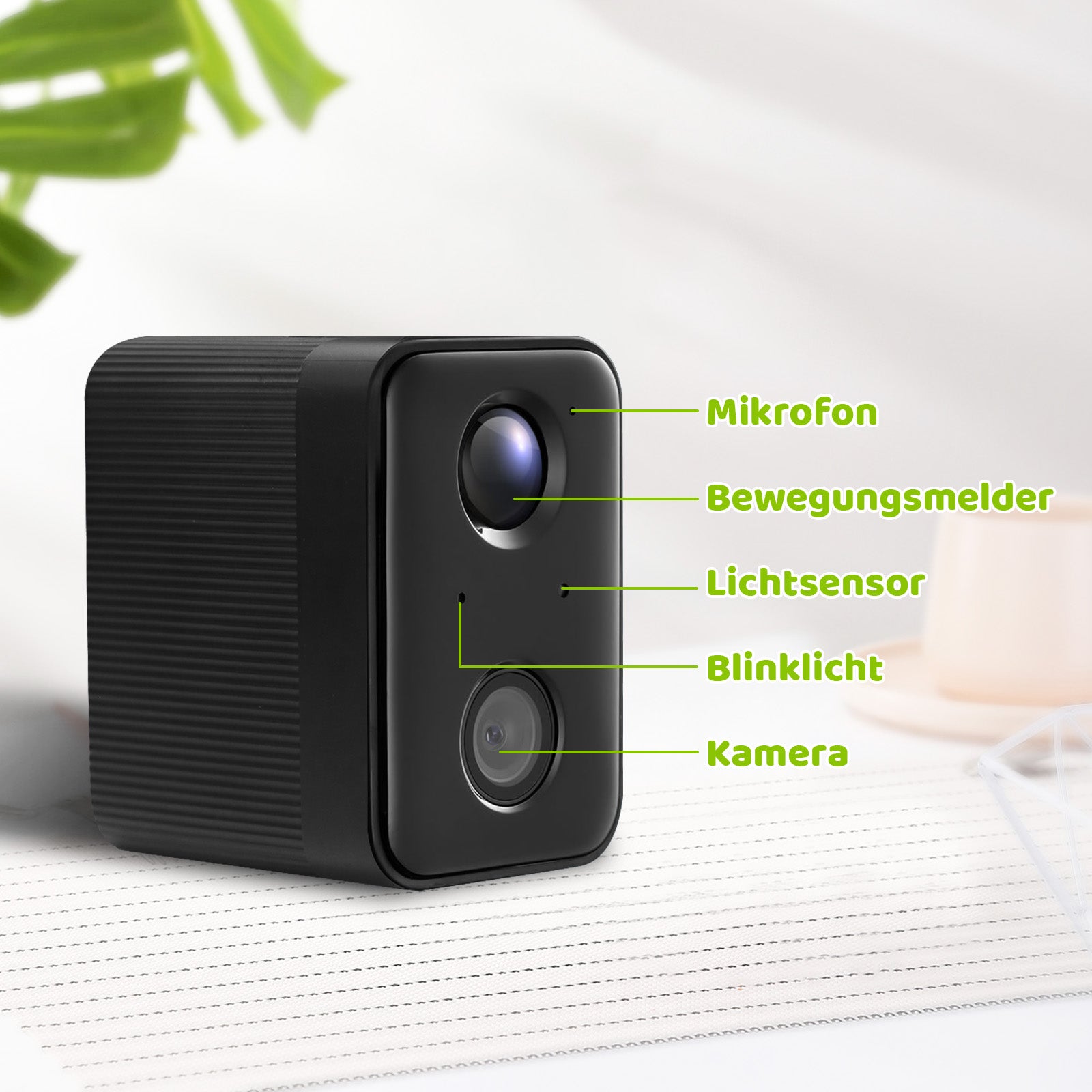 Schwarze kompakte Überwachungskamera mit zwei Linsen und grünen Beschriftungen (Mikrofon, Bewegungsmelder, Lichtsensor, Blinklicht, Kamera) auf hellem Hintergrund